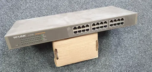 A disconnected TP-Link SF1024 network switch, propped up on a small cardboard box.